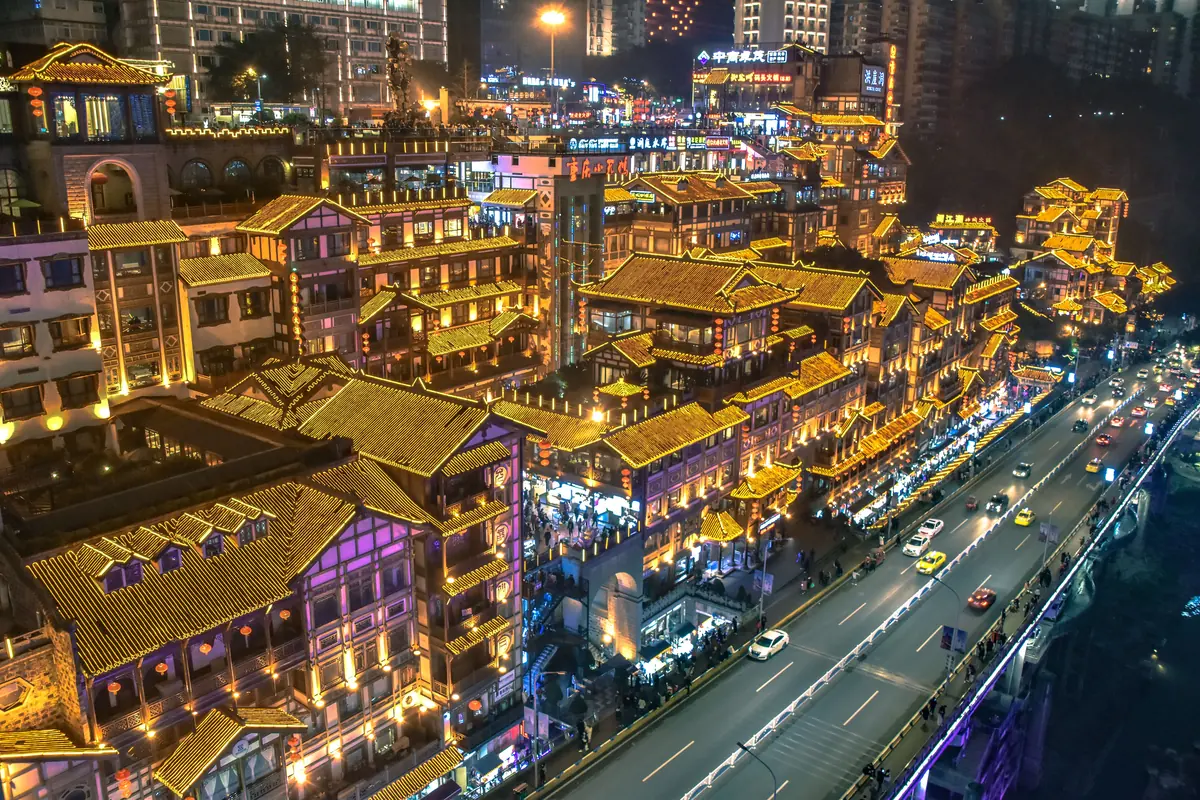 Aerial view of Hongya Cave's golden roofs above a busy road in Chongqing at night.