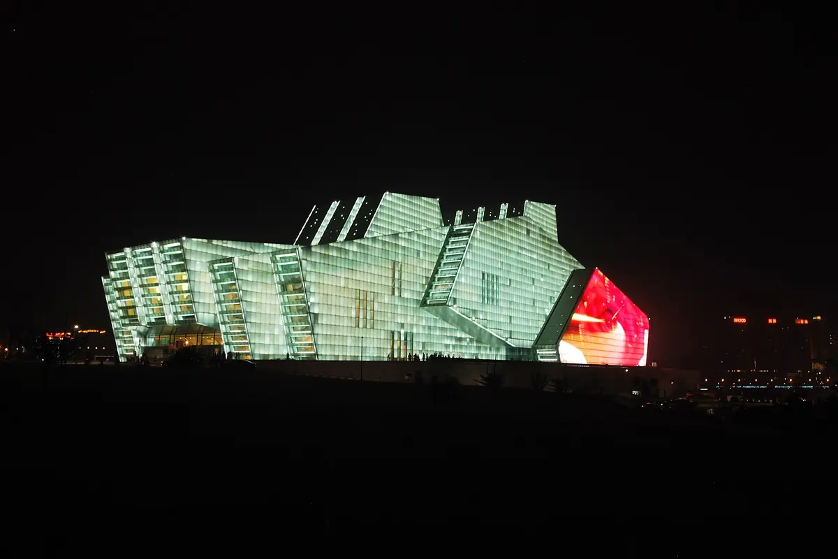 The Chongqing Grand Theatre, a large glass-faced building, lit green and red at night